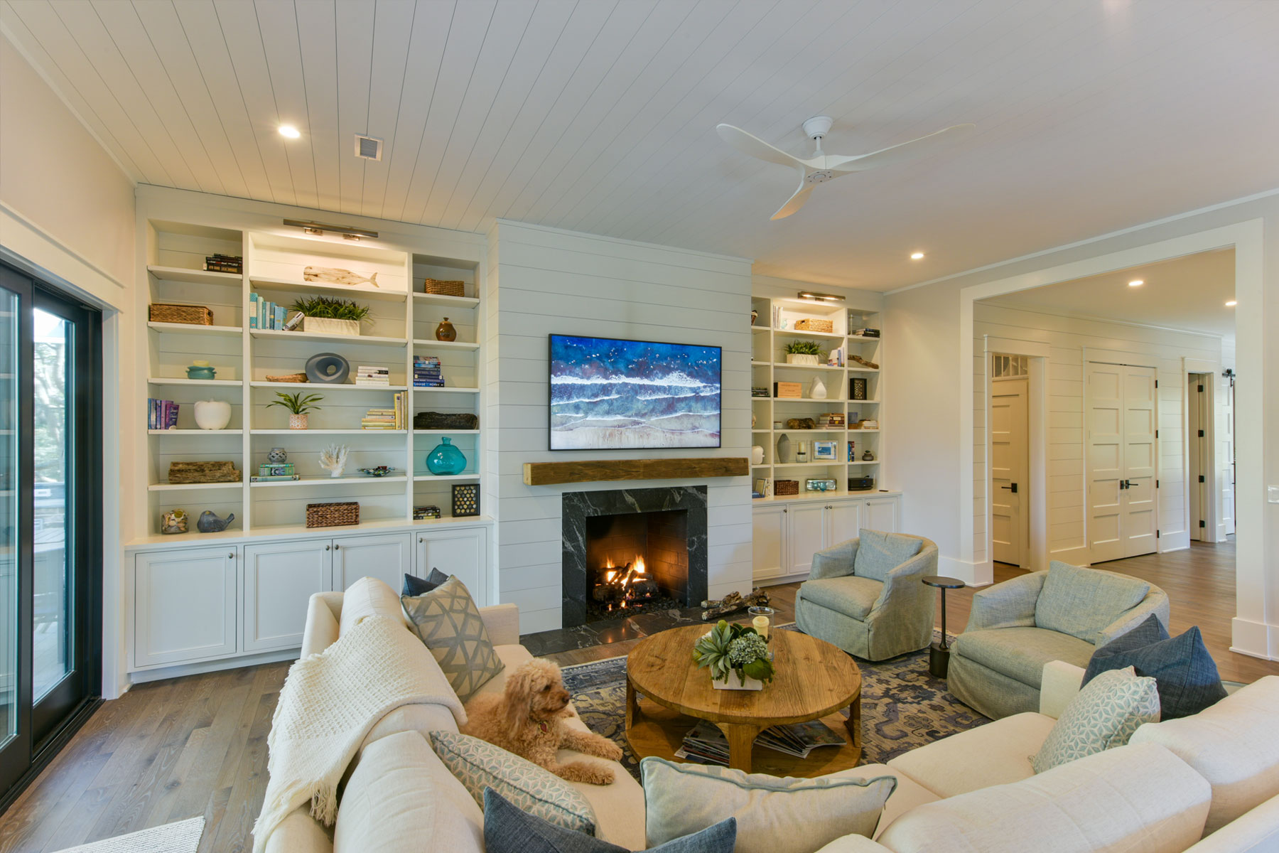 Coastal family room design with nickel gap walls, natural wood mantel, bookcases