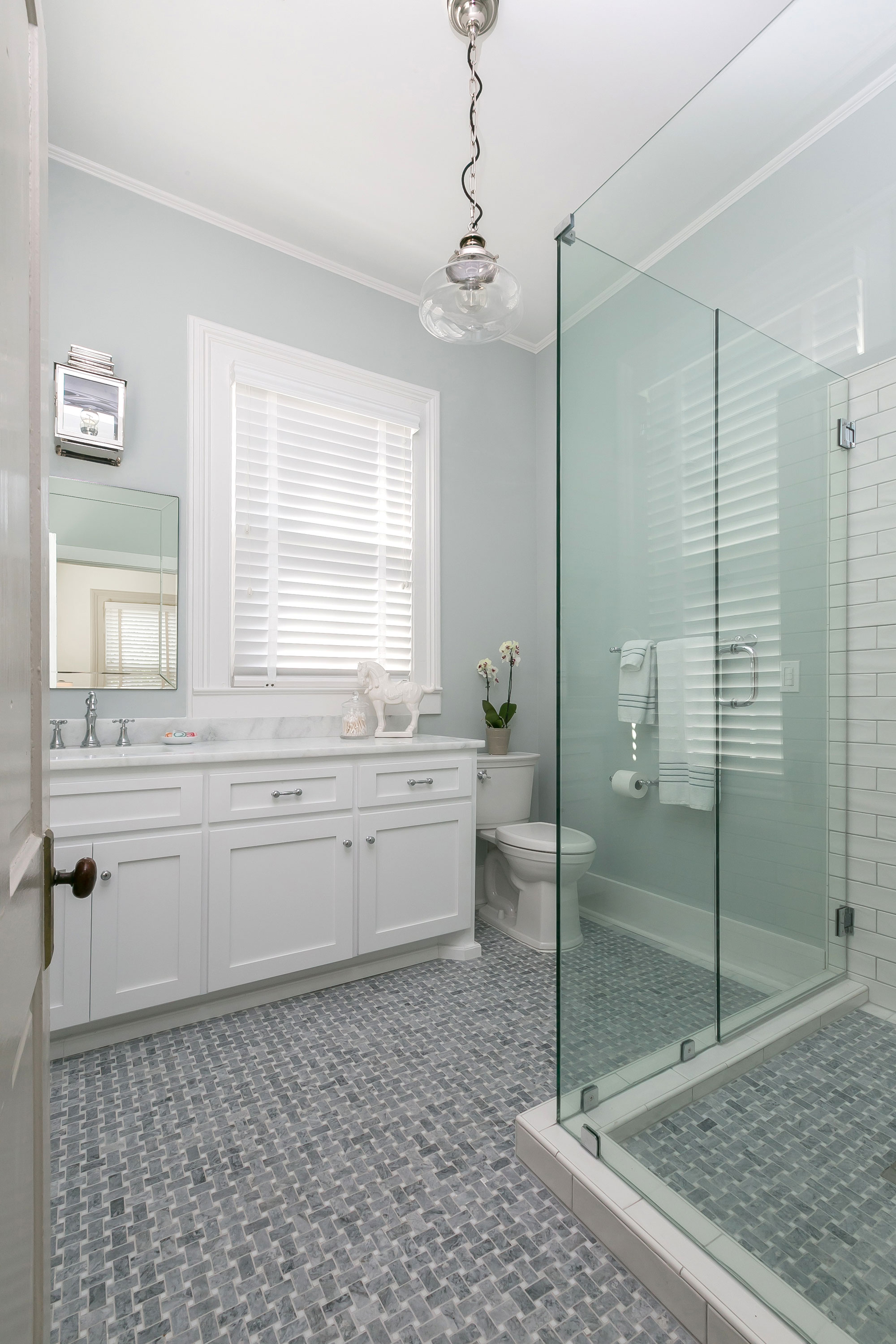 Marble basketweave tile, glass enclosed shower, vanity with offset mirror by window