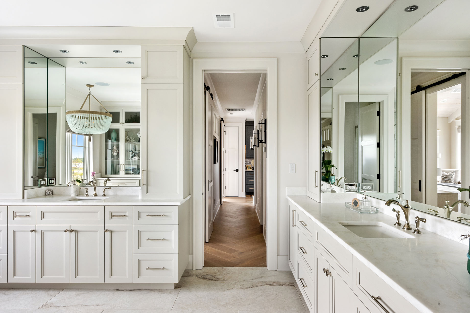 Large bathroom suite with separate vanities, marble, and hallway to closets with wide herringbone wood floor