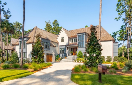 Custom designed luxury home with European influences and modern touches on elevated coastal home with stucco exterior and gray painted window dormers.