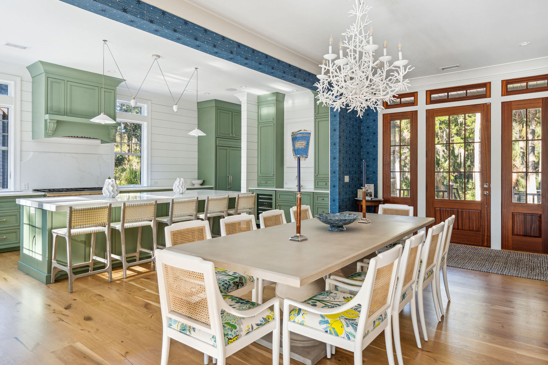 Large open dining area with 10 seat table (cane-back seats with upholstery bottoms) right next to large open kitchen. Blue, green, yellow palette contrasts medium and deep-toned stained wood
