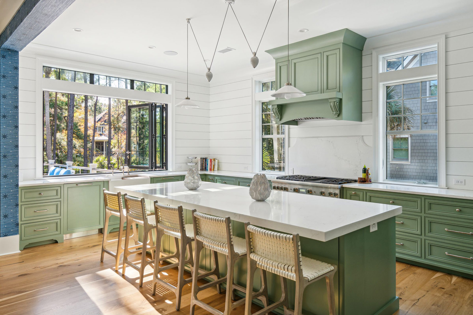 Coastal Carolina kitchen with mossy green cabinets, large island, and accordion window at counter height opening to the rear pool deck